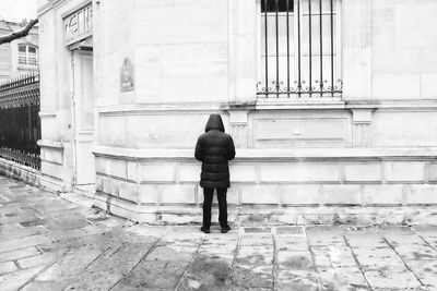 Rear view of man walking on footpath against building