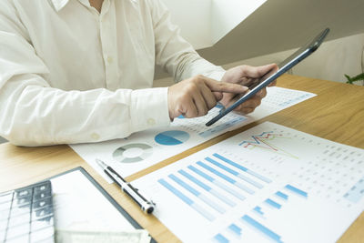 Midsection of man with digital tablet analyzing chart on table