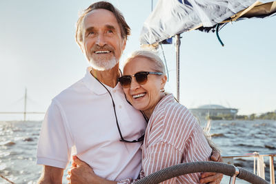 Smiling senior couple standing on boat in sea against sky