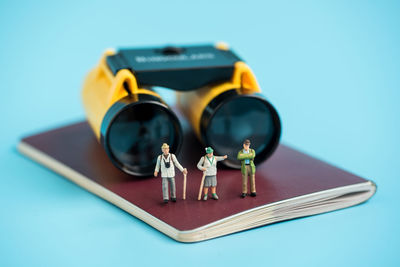 Close-up of hiker figurines on passport with binoculars against blue background