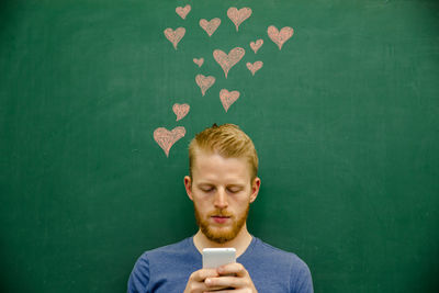 Young man using mobile phone with hear shapes on blackboard