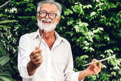 Portrait of man holding paintbrush against trees