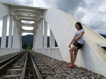 Low angle view of young woman leaning on built structure by railroad track