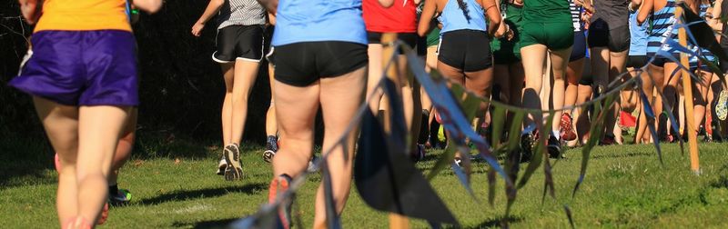 Rear view of girls running uphill in a 5k on grass in a park