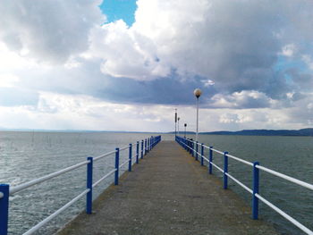 Empty jetty leading to sea against cloudy sky