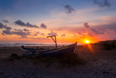 Boat moored on beach against sky during sunset