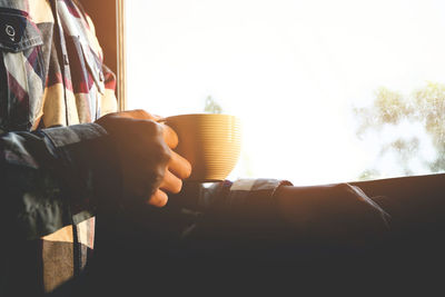 Man holding coffee cup by window