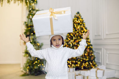 Portrait of a boy a child in a white sweater holding a gift box at the christmas tree