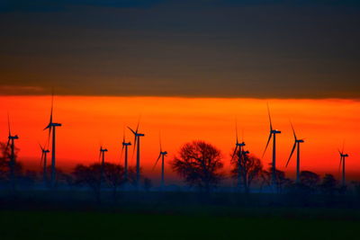 Silhouette windmill on field against orange sky