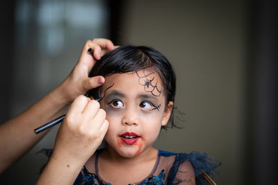 Mother painting daughters face. halloween party.
