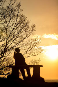 Silhouette man sitting on railing against orange sky