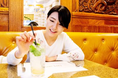 Young woman holding drink while sitting on table at restaurant
