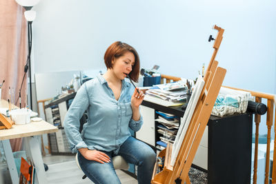 Concentrated pensive  caucasian woman artist drawing with pencil on canvas at home art studio