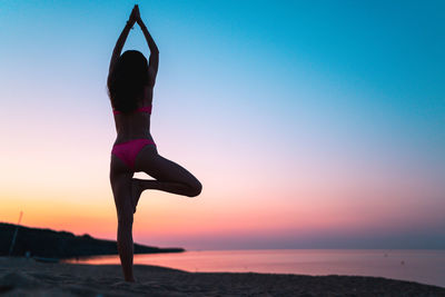 Woman standing at beach against sky during sunset