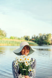 Portrait of smiling woman against lake against sky