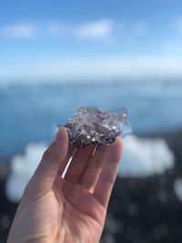 Cropped hand holding ice against sky