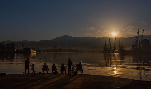 Rear view of silhouette people fishing in lake against sky during sunset