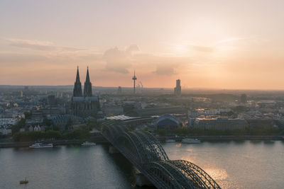 Bridge over river in city against sky during sunset