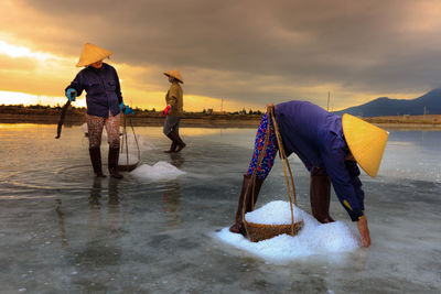 Men fishing on beach against sky during sunset