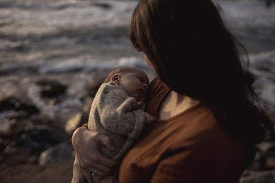 Mother carrying newborn baby boy at beach