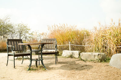 Empty chairs and table against trees on field against sky