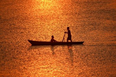 Silhouette people in boat against sky during sunset