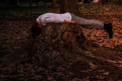 Side view of woman lying on tree stump at park