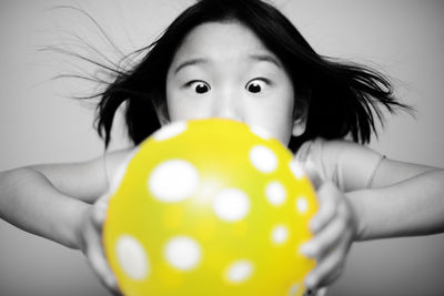 Girl blowing yellow balloon against wall