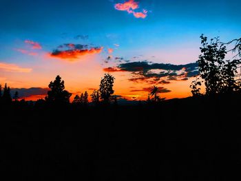 Silhouette trees against dramatic sky during sunset