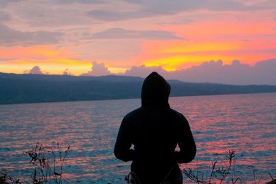 Rear view of silhouette man standing against orange sky