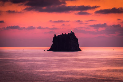 Scenic view of rock in sea against sky during sunset