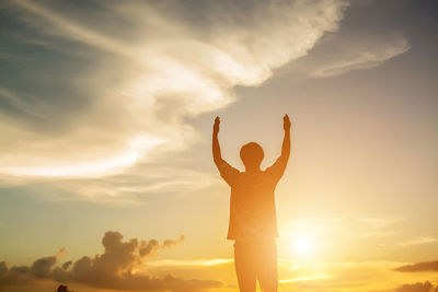 Silhouette man with arms raised standing against sky during sunset