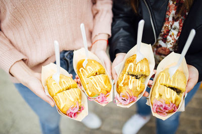 Two women holding stuffed potatoes with onion and sauce. street food. foodtruck. focus on food