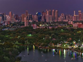 Illuminated buildings by river against sky in city at night