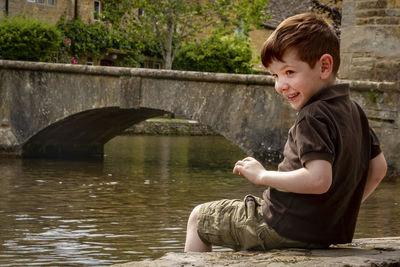 Side view of smiling boy sitting by lake