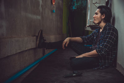 Side view of young man looking away while sitting on wall