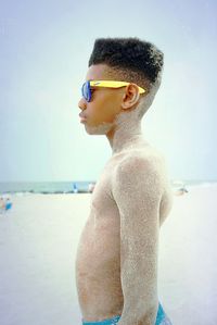 Side view of young man wearing sunglasses standing on beach
