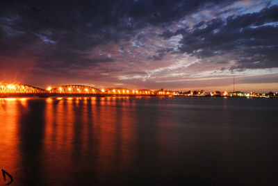 Illuminated city at waterfront during sunset