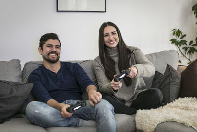 Happy couple playing video game while sitting on sofa at home