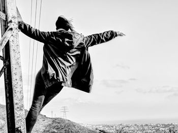 Rear view of carefree woman standing on metallic tower against sky