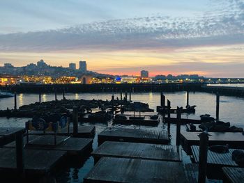 Bridge over river by buildings against sky during sunset