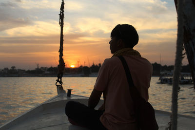 Man sitting in boat on lake during sunset