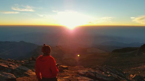 Rear view of woman standing on mountain during sunset