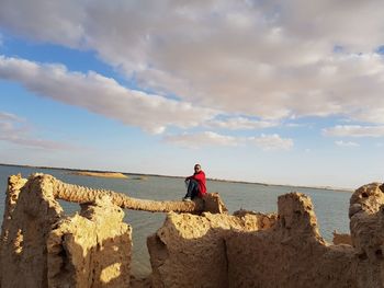 Woman on rock by sea against sky