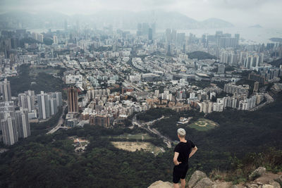 High angle view of man looking at cityscape while standing on rock