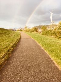 Road amidst field against rainbow in sky