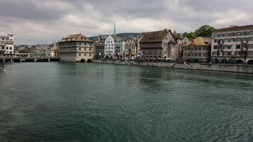 View of buildings by river against cloudy sky