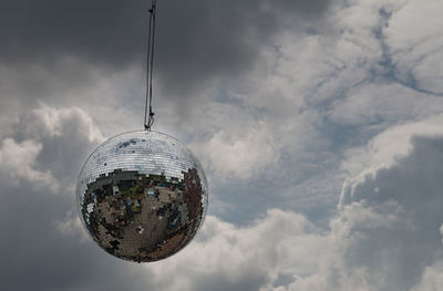 Low angle view of disco ball hanging against cloudy sky