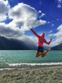 Woman jumping on beach against sky