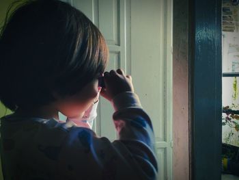 Rear view of boy photographing through window